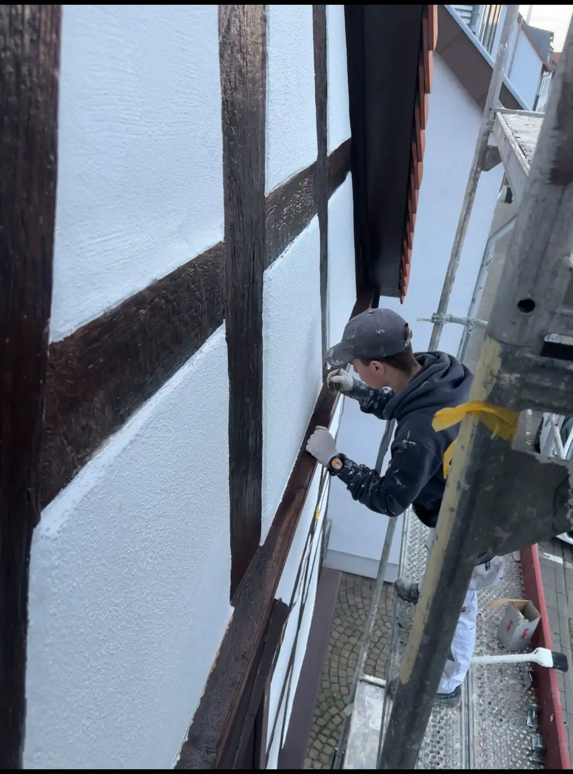 Handwerker auf dem Gerüst beim Streichen der Fachwerkbalken an der Fassade