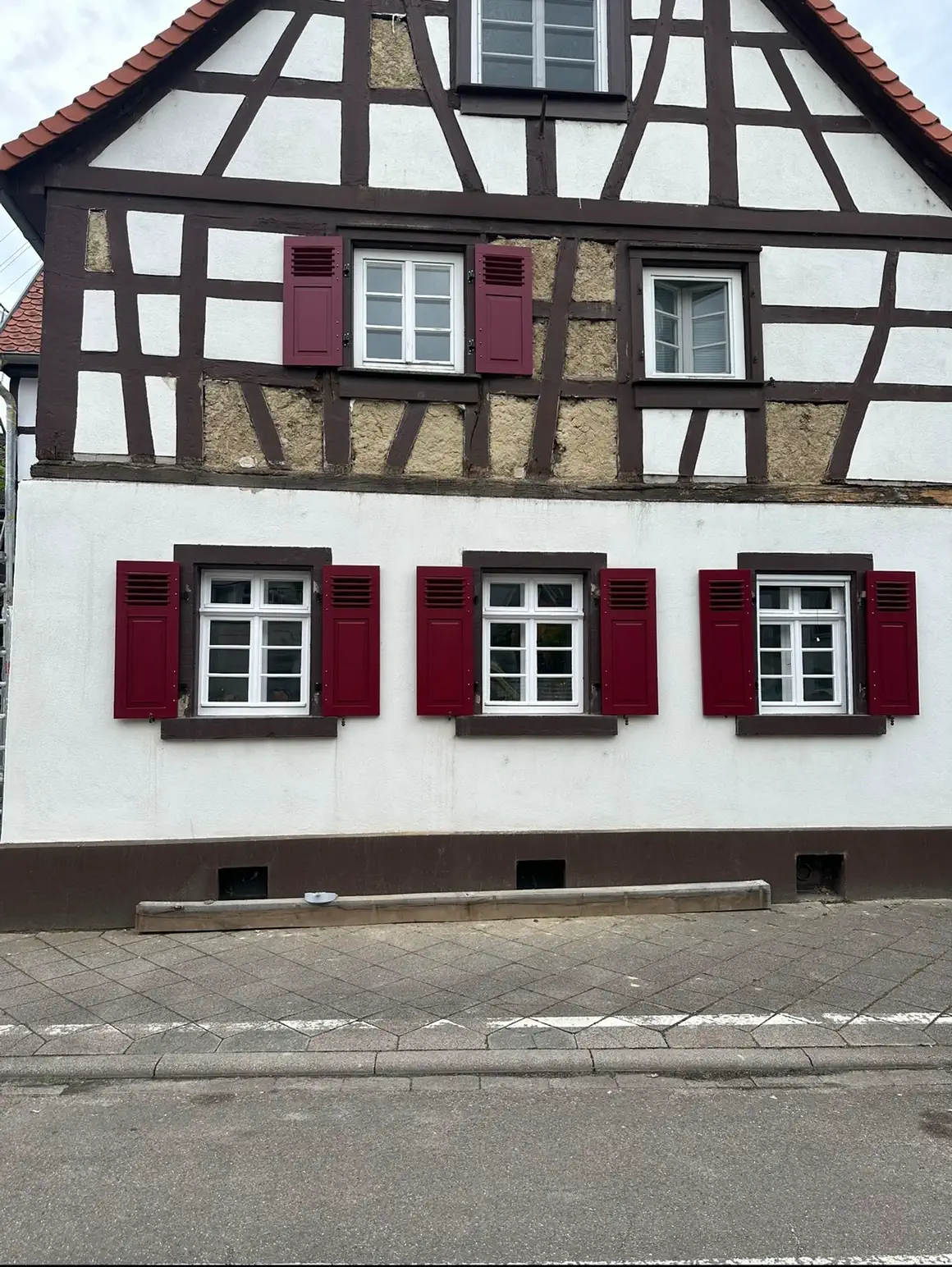 Fertig sanierte Fachwerkfassade mit Kalkanstrich und roten Fensterläden