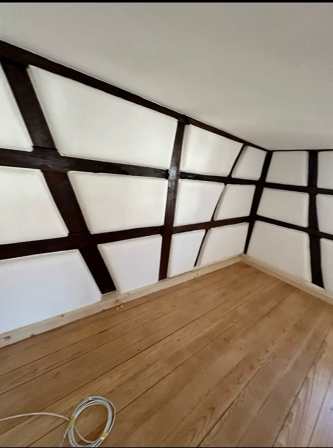 Wohnraum mit dunklem Fachwerk, weissem Kalkputz und geöltem Dielenboden